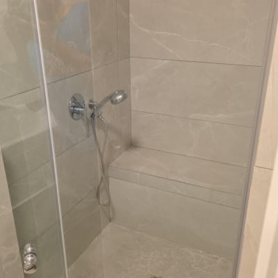מקלחון זכוכית נקי ומבריק עם חיפוי אריחים וספסל מובנה בחדר רחצה