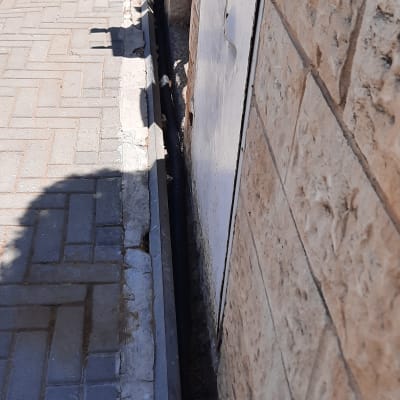 צינור שחור ליד קיר אבן על מדרכה