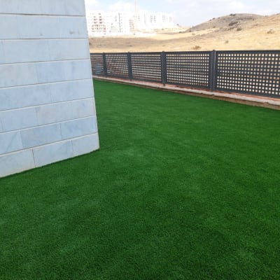 דשא סינתטי ירוק ליד קיר וגדר מתכת