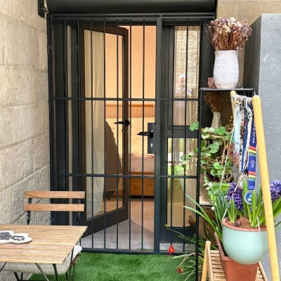 דלת עם סורגים, שולחן וכיסאות, עציצים עם פרחים