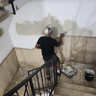 אדם צובע קיר במדרגות עם מברשת ודלי צבע