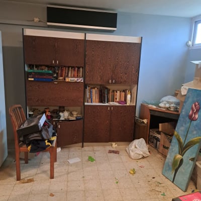 חדר מבולגן עם ארון ספרים וציוד פזור לפני תהליך סידור הבית