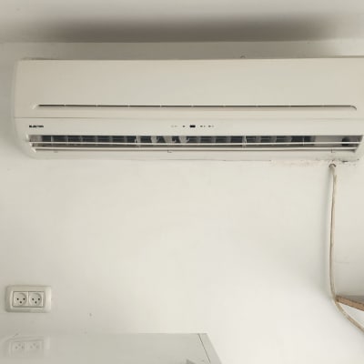 מזגן מותקן על קיר לבן מעל מקרר קטן