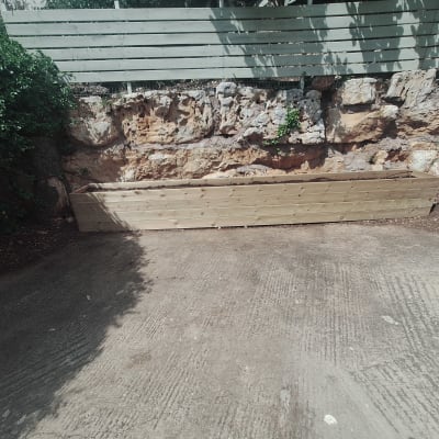 אדנית עץ ריקה ליד קיר אבן בגינה