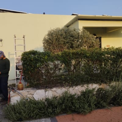 אדם עובד בגינה עם כלים ליד שיחים וגדר חיה