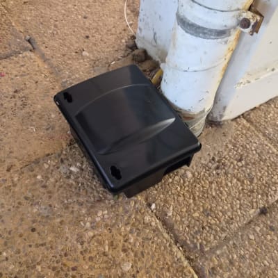 תיבת האכלה מפלסטיק שחור להדברת מכרסמים שהוצבה מחוץ למבנה