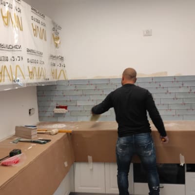 אדם מתקין אריחים על קיר מטבח עם כלים