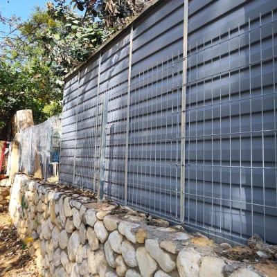 גדר מתכת על קיר אבנים עם צמחייה מסביב