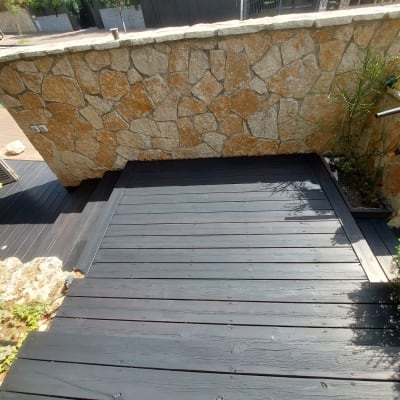 דק עץ כהה ליד קיר אבן בגינה