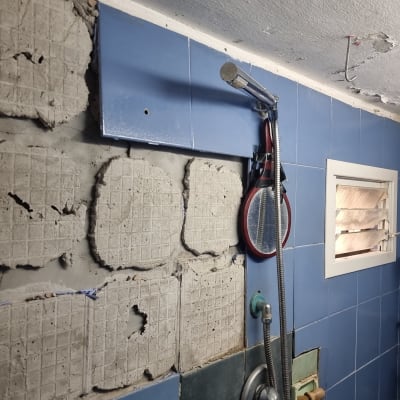 קיר אמבטיה עם אריחים שבורים ותיקוני טיח