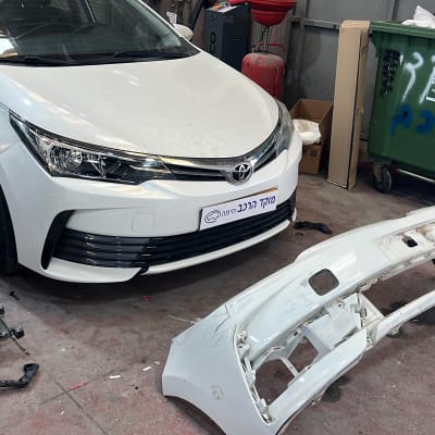 רכב לבן עם פגוש מפורק במוסך תיקונים.