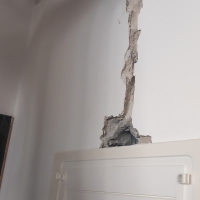 יד מחזיקה מקדחה ליד לוח חשמל בקיר