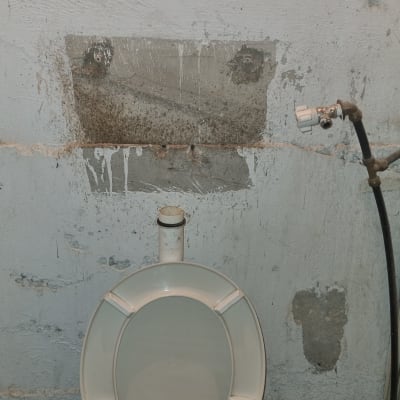 אסלה עם צינור מים וברז על קיר בטון