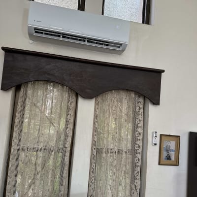 מזגן מותקן על קיר מעל חלון עם וילון תחרה