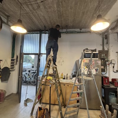 חשמלאי עובד על תקרה עם סולם וכלי עבודה