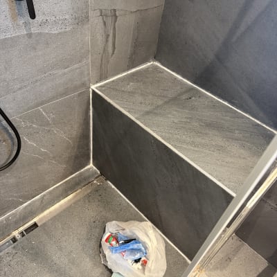 פינת מקלחת עם אריחים אפורים ושקית אשפה
