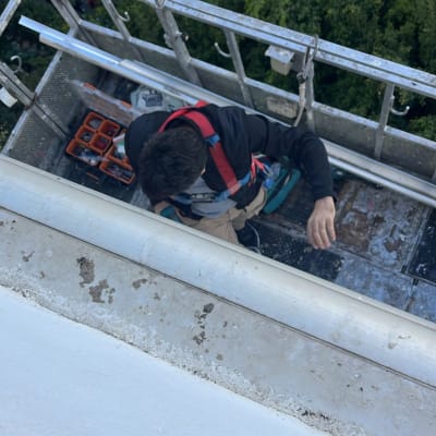 אדם על פיגום עם כלים ליד תריסים