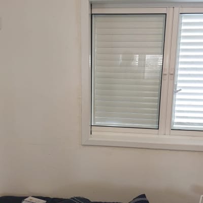 חלון עם תריסים סגורים ומיטה עם כריות