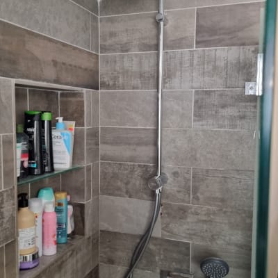 ראש מקלחת עגול עם צינור מתכת על קיר אריחים