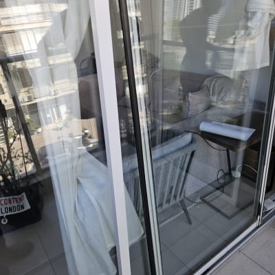 חלון זכוכית עם וילון לבן ומרפסת ברקע