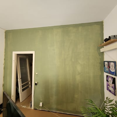 קיר צבוע בירוק עם דלת פתוחה וציורים תלויים