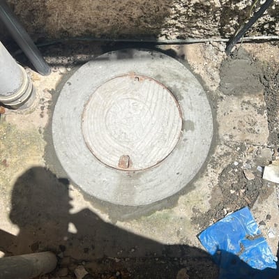 מכסה ביוב עגול על רצפת בטון עם צינור סמוך