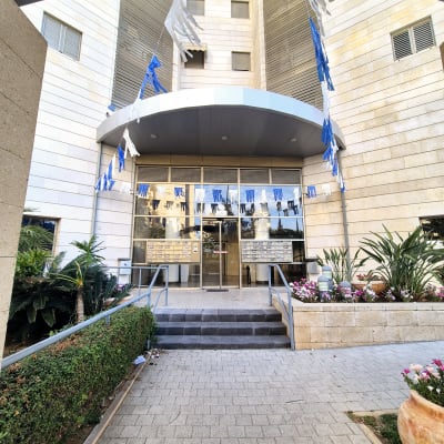 כניסה לבניין עם דגלים כחולים ולבנים, עציצים ופרחים