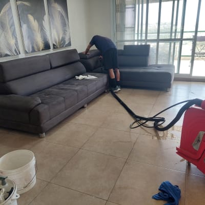 אדם מנקה ספה עם מכונת ניקוי אדומה