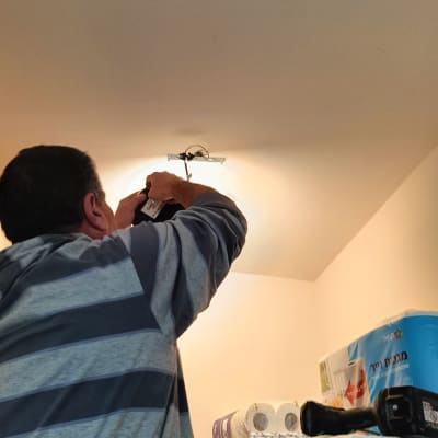 חשמלאי מתקין גוף תאורה בתקרה עם מברגה