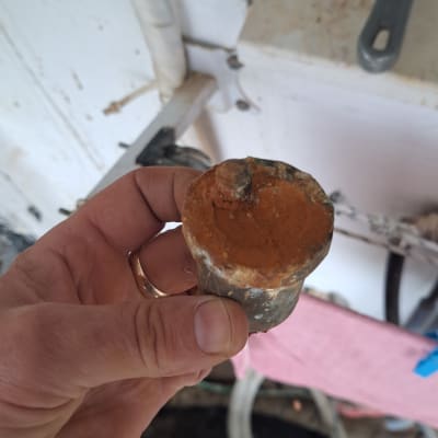 חלק מתכת חלוד מוחזק ביד ליד צינורות