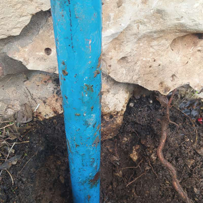 צינור כחול תקוע באדמה ליד קיר אבן