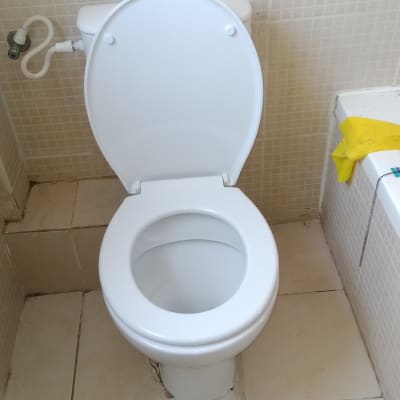 אסלה לבנה עם צינור מים מחובר לקיר