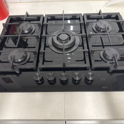 כיריים גז שחורות עם שישה מבערים על משטח שיש.