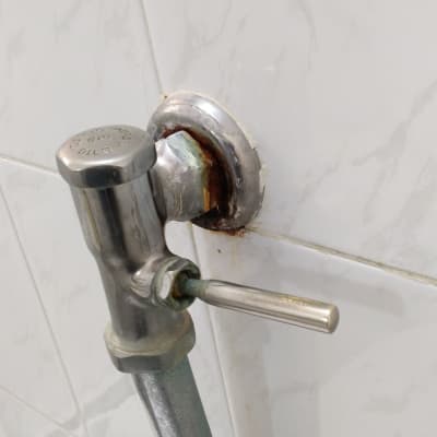 ברז מתכת עם חלודה על קיר אריחים לבן