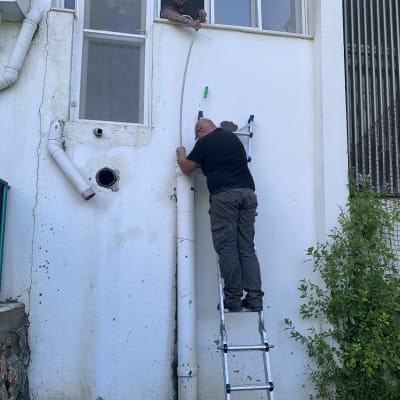 אדם על סולם מתקן צינור ליד חלון