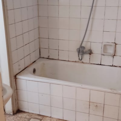 חדר אמבטיה ישן עם אריחים מתקלפים וקירות מוכתמים