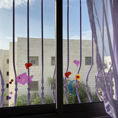 מדבקות צבעוניות על סורגי חלון עם וילון סגול