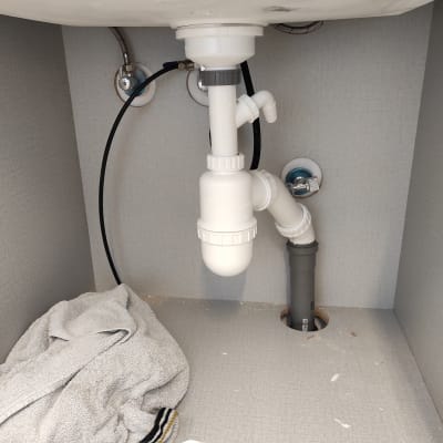 צנרת פלסטיק מתחת לכיור עם מגבת על הרצפה