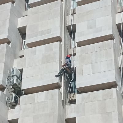 אדם עם קסדה אדומה עובד על קיר בניין גבוה