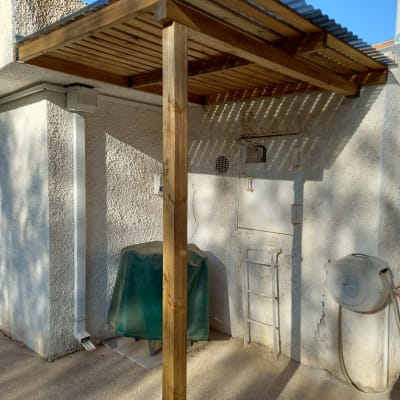 פרגולה מעץ עם גג מתכת ליד קיר חיצוני