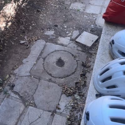 שוחת ביוב מבטון בחצר לצד מדרגה עם קסדות אופניים