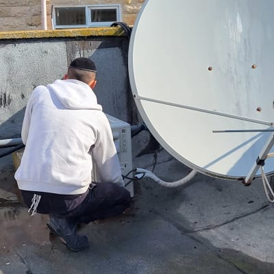 אדם עובד על מזגן על גג ליד צלחת לוויין