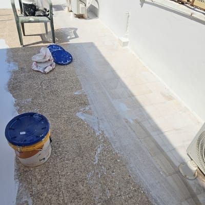 מריחת חומר איטום על רצפת מרפסת עם דלי וצבע לבן