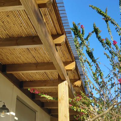 פרגולה מעץ עם גג במבוק לצד עץ פורח