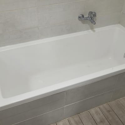 אמבטיה לבנה עם ברז קיר ותיק כלים על הרצפה