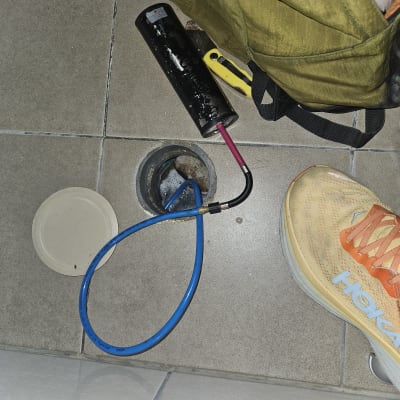 צינור כחול וכלי עבודה ליד פתח ניקוז ברצפה