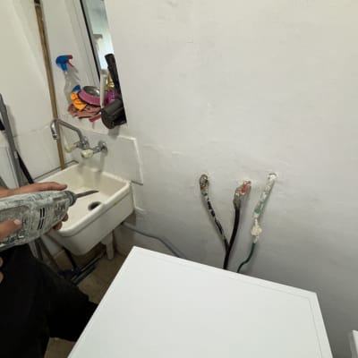 אדם מחזיק מקדחה ליד כיור וצינורות חשופים