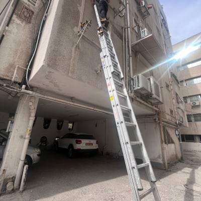 אדם על סולם מתקין תריסים חיצוניים בבניין