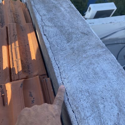 אצבע מצביעה על סדק בגג בטון ליד רעפים