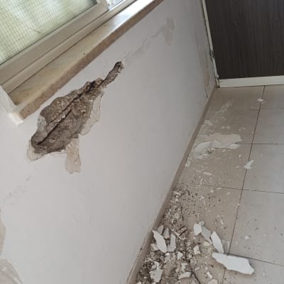 קיר פנימי עם טיח מקולף ונזק לבטון מתחת לחלון לפני תיקון וצביעה